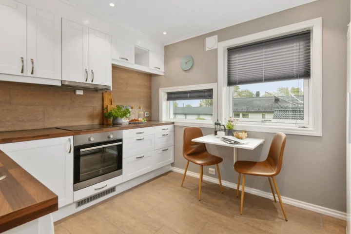Modern kitchen interior with white cabinets, wooden countertops, integrated appliances, and a small dining area.