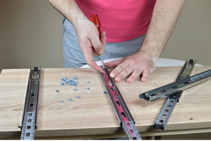 Closeup of man&rsquo;s hands installing drawer slides on a wooden cabinet.